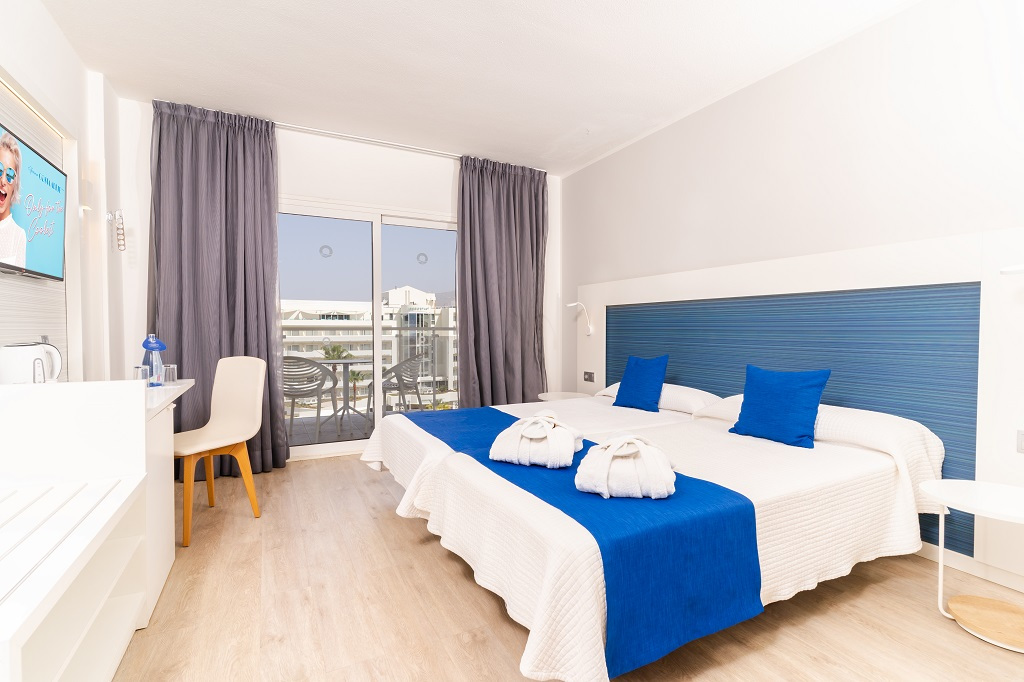 Camera d'hotel a Tenerife con letti gemelli, cuscini blu e vista città.