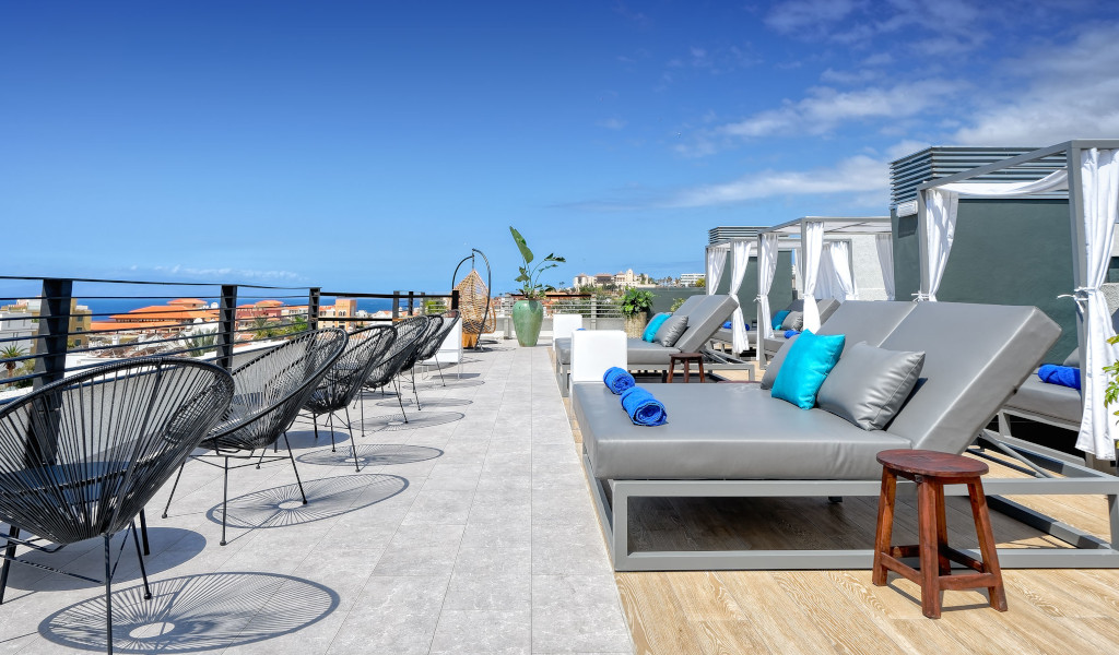 Terrazza con lettini e vista su Costa Adeje, Tenerife, sotto cielo sereno.