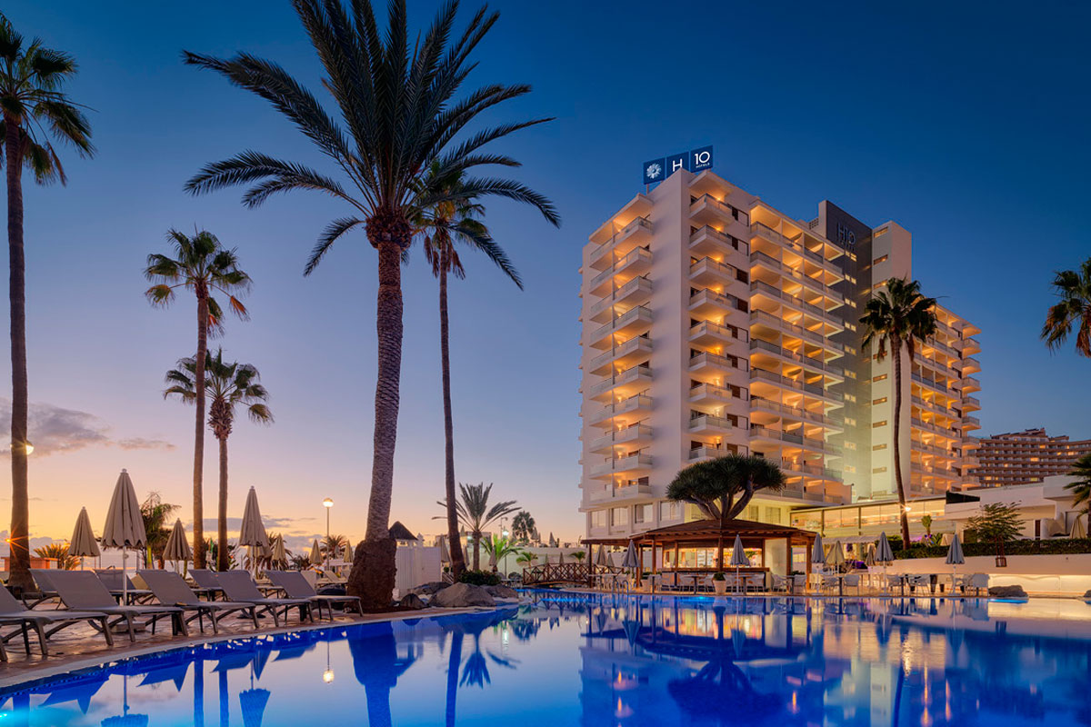 Hotel con piscina al tramonto a Tenerife, circondato da palme e lettini.