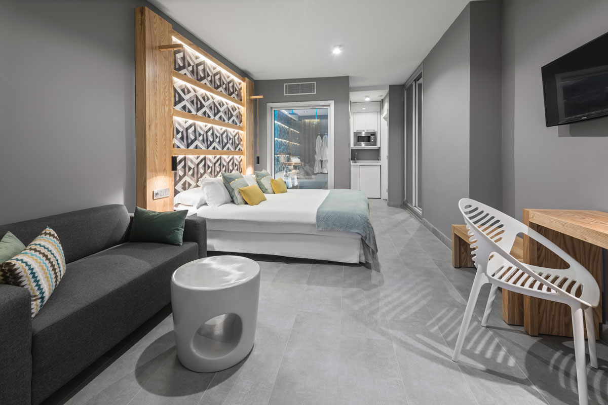 Camera moderna con letto matrimoniale, divano grigio e angolo cottura a Tenerife.