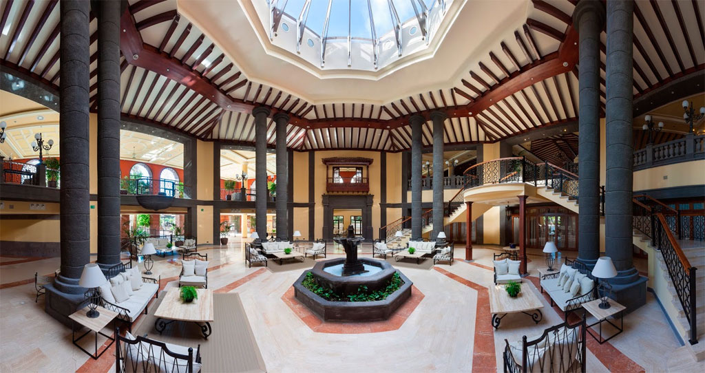 Interno spazioso di un hotel a Tenerife con soffitto in vetro e colonne grigie.