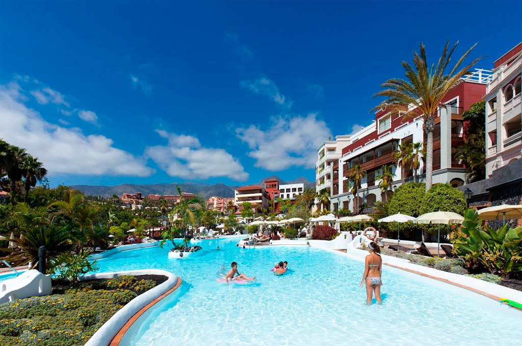 Piscina di un hotel a Tenerife circondata da palme e lettini con sfondo montuoso.