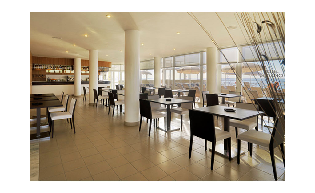 Sala da pranzo luminosa con tavoli e sedie nere a Hotel Medano, Tenerife.