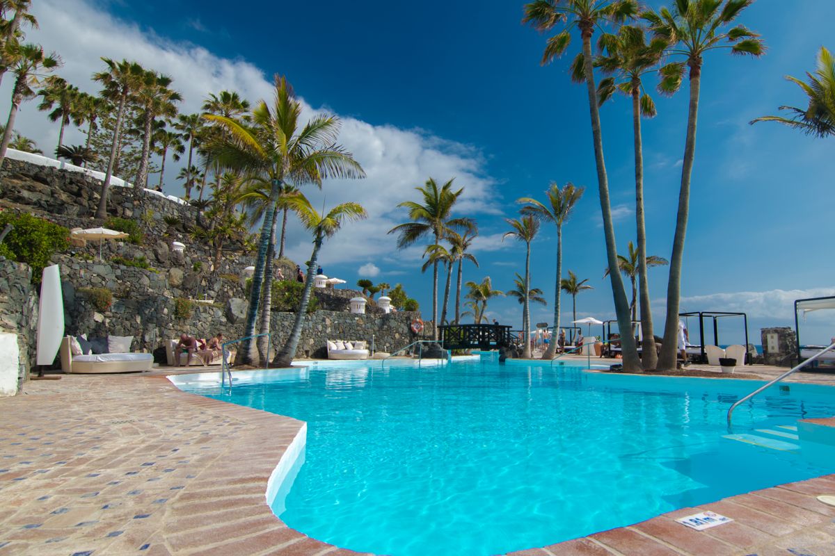 Piscina serena circondata da palme a Tenerife, con cielo blu limpido.