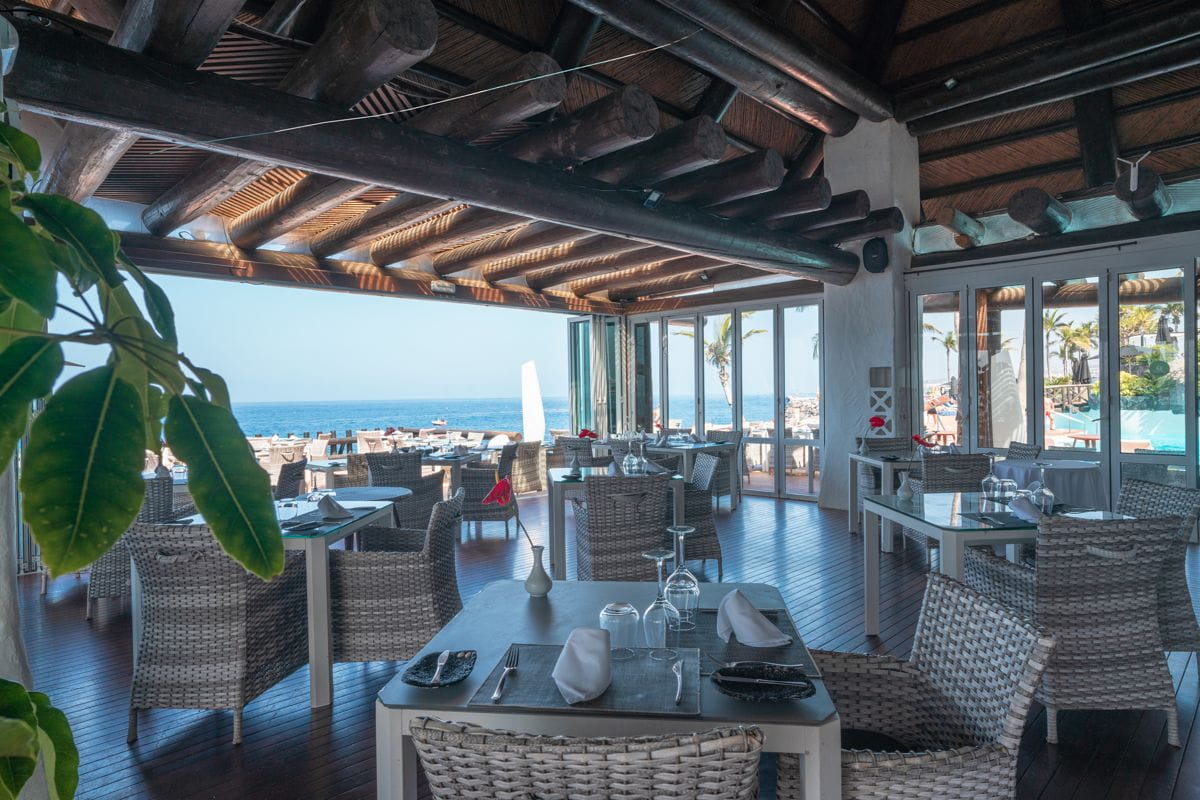 Sala da pranzo con vista mare a Tenerife, tavoli apparecchiati e piante verdi.