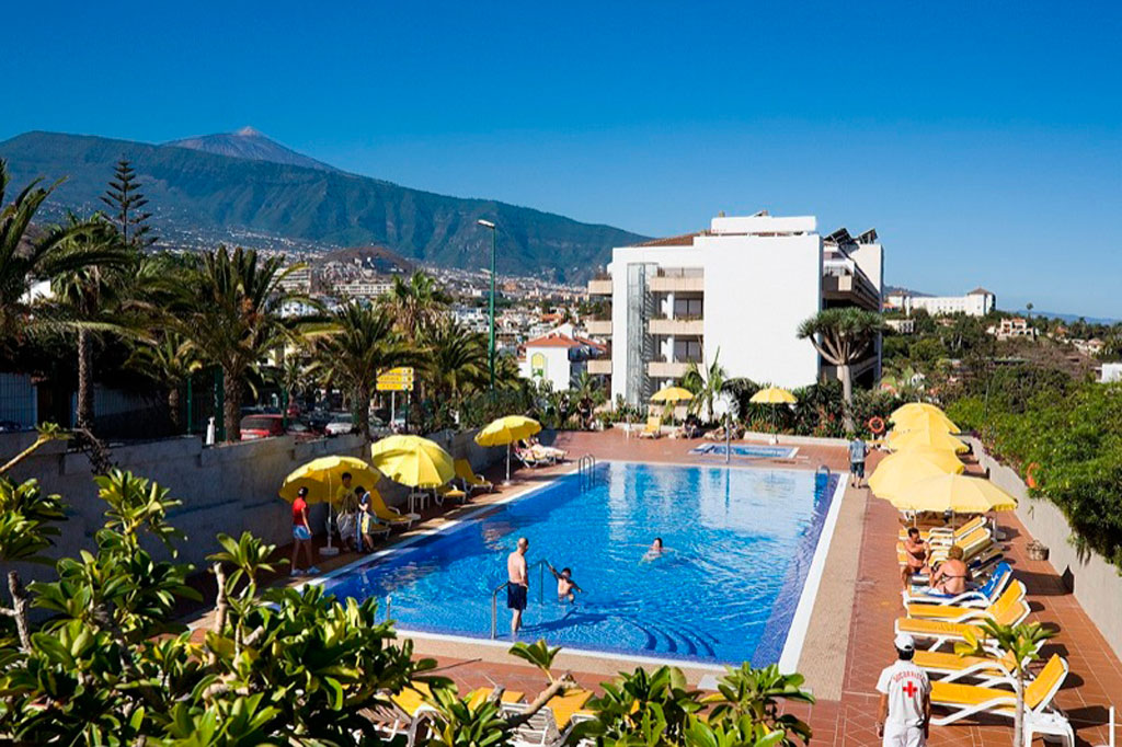 Piscina all'aperto con ombrelloni gialli e montagna vista a Puerto de la Cruz, Tenerife.