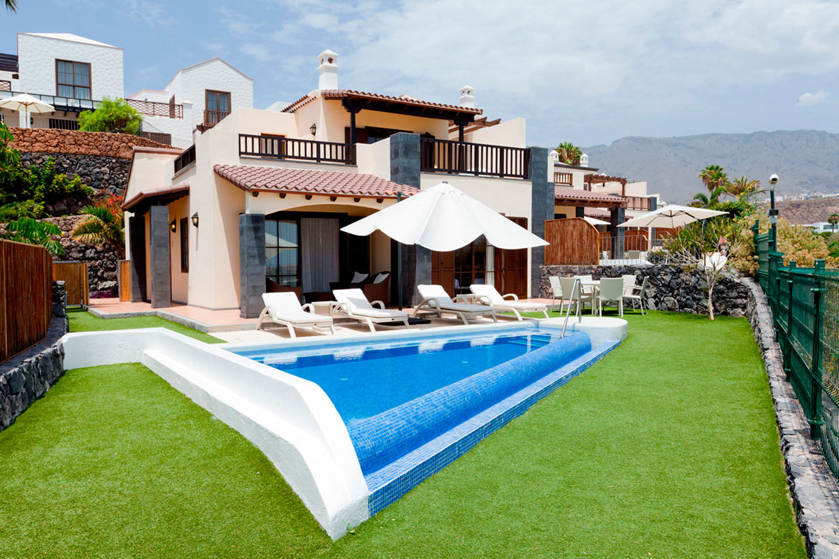 Villa con piscina e lettini a Tenerife, circondata da giardino e montagna sullo sfondo.
