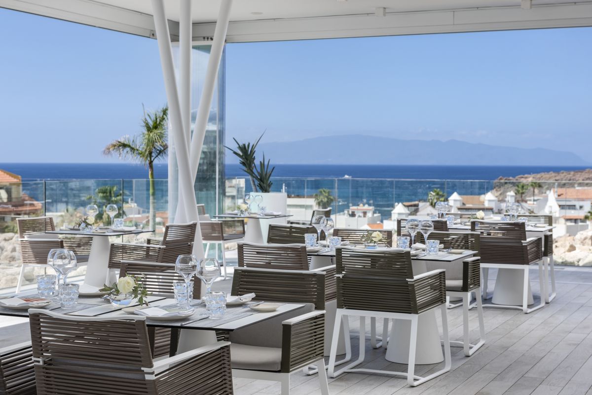 Ristorante con vista mare a Tenerife, tavoli apparecchiati e palme sullo sfondo.