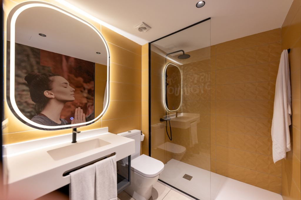 Bagno con doccia, lavandino, specchio illuminato e fotografia di una donna che medita a Tenerife.