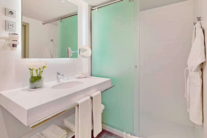 Bagno moderno con lavabo, specchio, doccia in vetro e asciugamani bianchi a Tenerife.