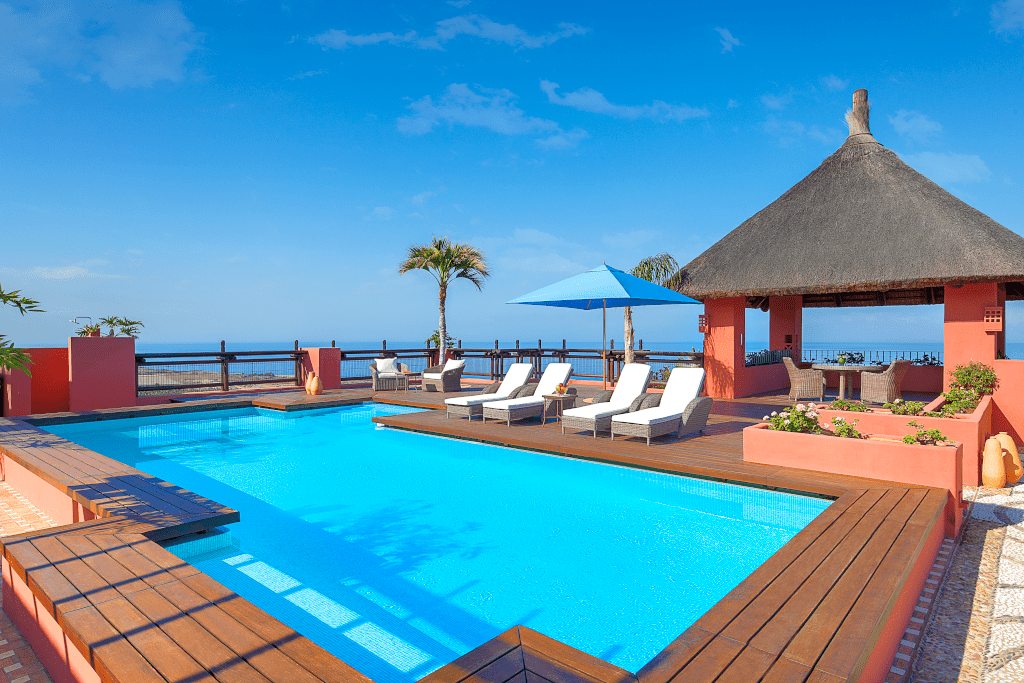 Piscina con lettini e ombrellone azzurro a Tenerife, vista mare sullo sfondo.