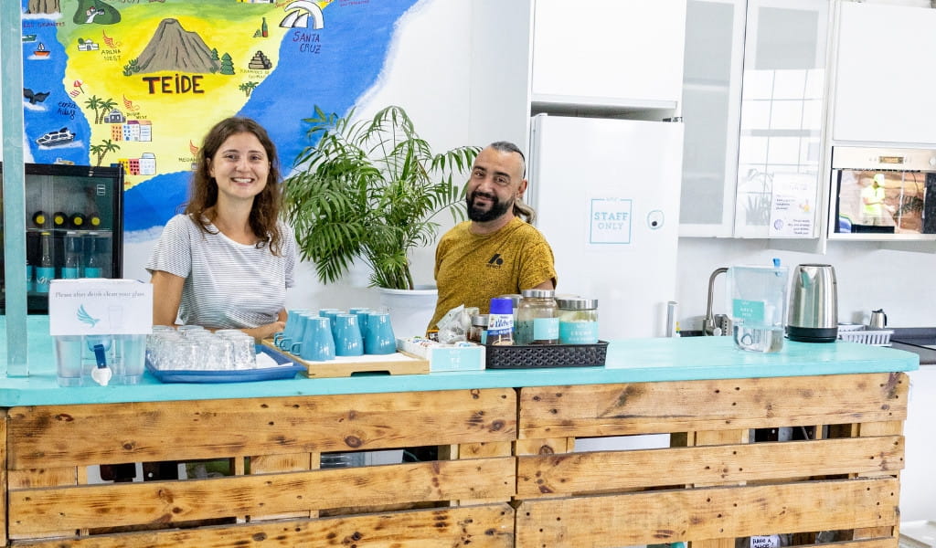 Due persone dietro un bancone di un bar con una mappa di Tenerife sullo sfondo.