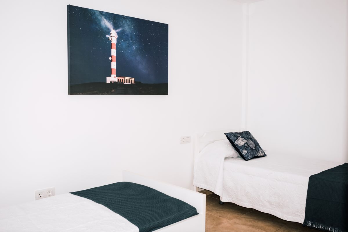 Due letti singoli con un quadro del faro di Tenerife sul muro.