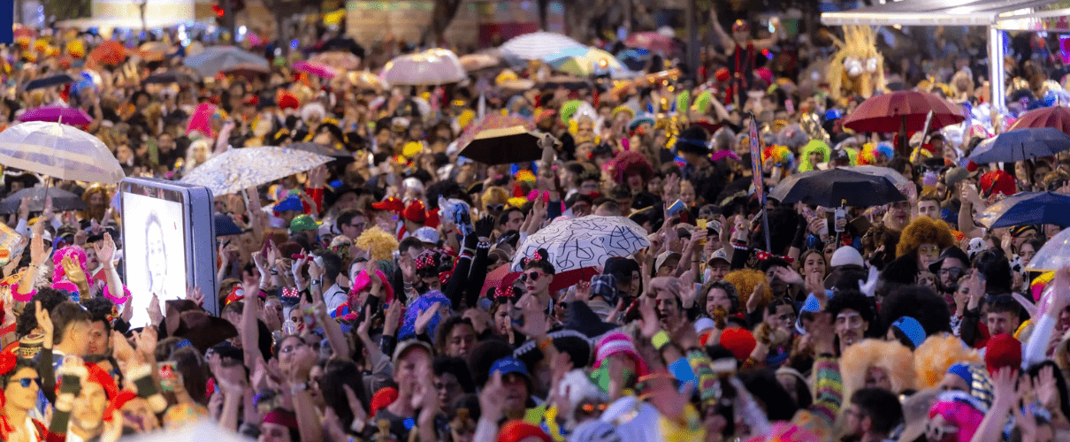 Folla festante al carnevale di Santa Cruz de Tenerife con ombrelli e costumi colorati.