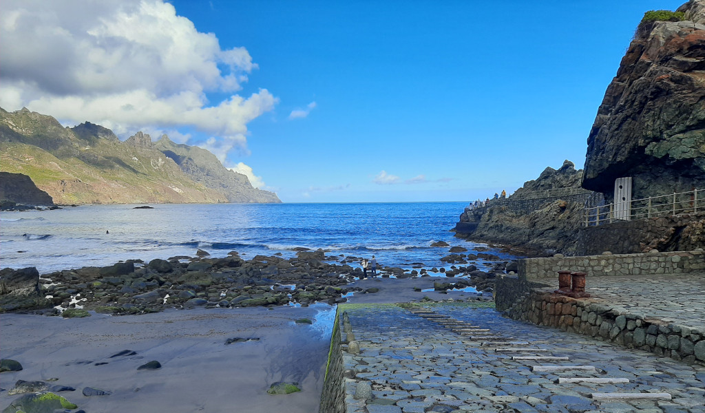 Spiaggia rocciosa con scogli e montagne a Tenerife sotto un cielo blu.