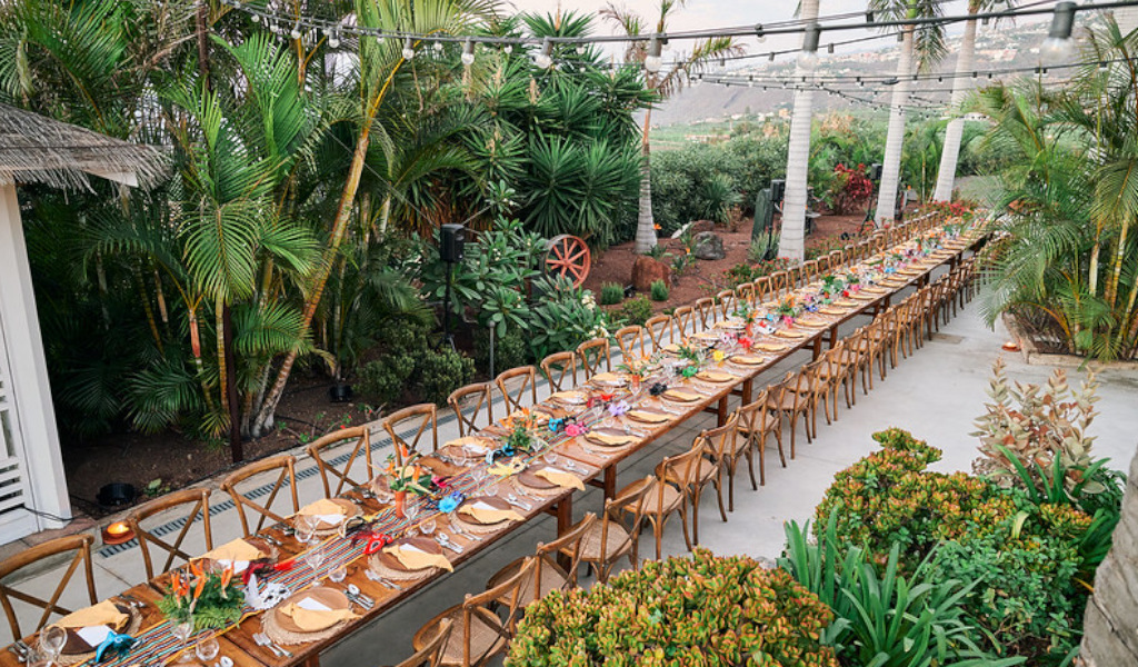 Un lungo tavolo decorato per eventi all'aperto a Tenerife, circondato da palme e vegetazione.