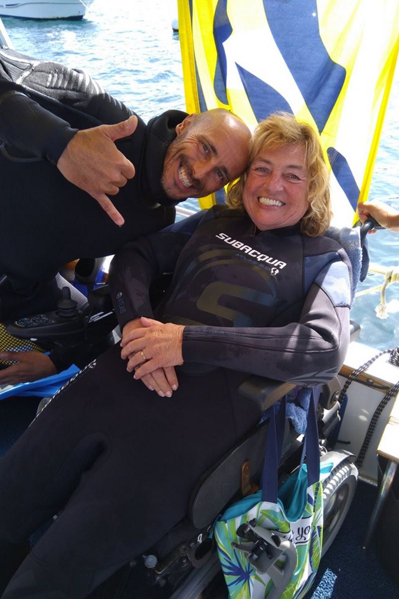 Persone in tute da subacqueo sorridenti su sedia a rotelle vicino al mare a Tenerife.