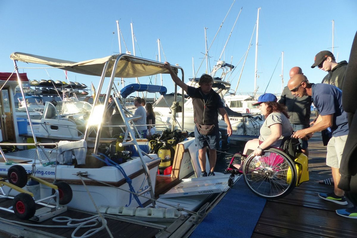Persona in sedia a rotelle che sale su una barca a Tenerife con l'aiuto di diverse persone.