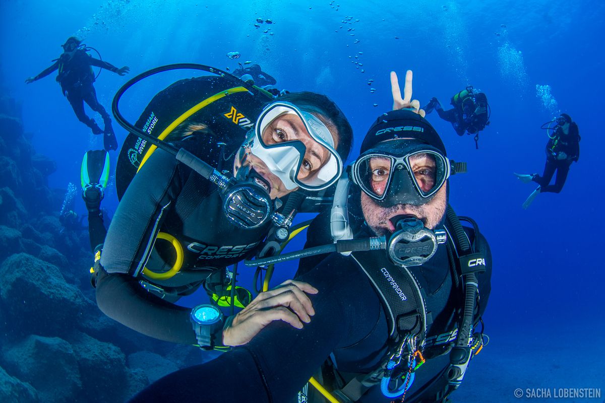 Subacquei che sorridono sott'acqua a Tenerife con altri sullo sfondo.