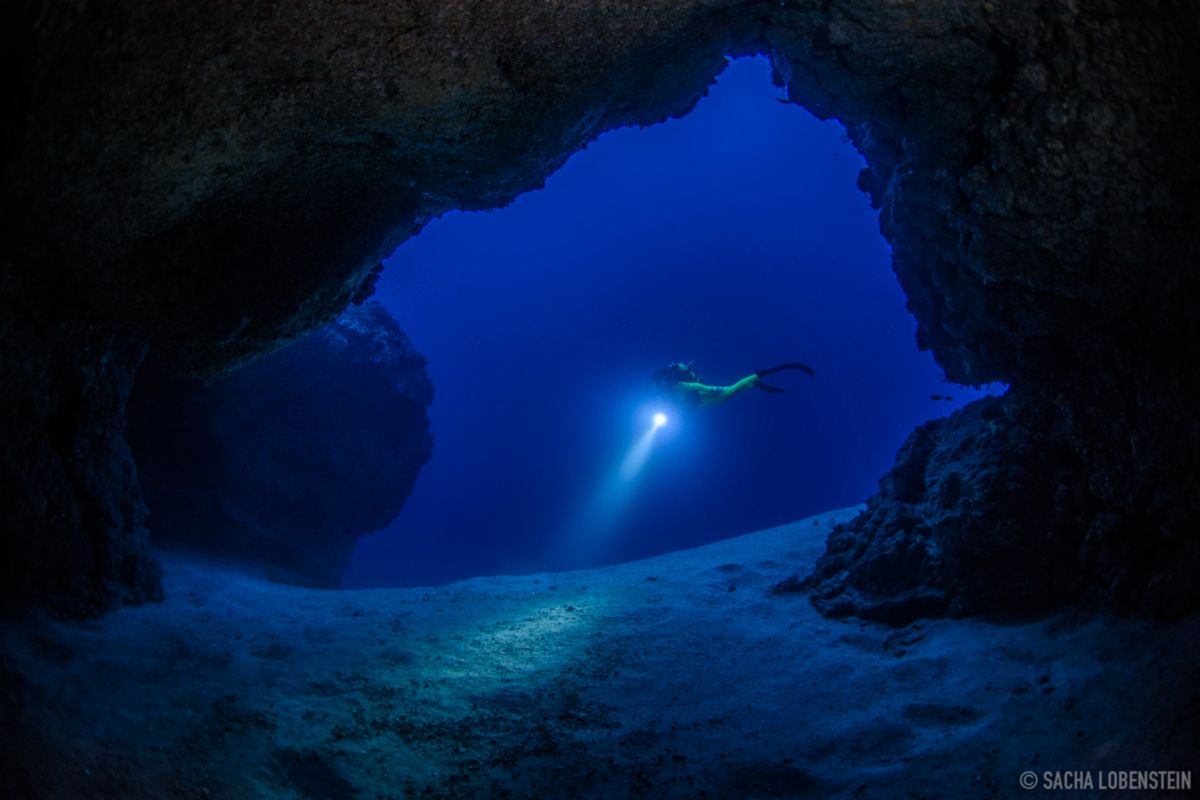 Subacqueo in grotta che illumina il fondale oceanico a Tenerife.