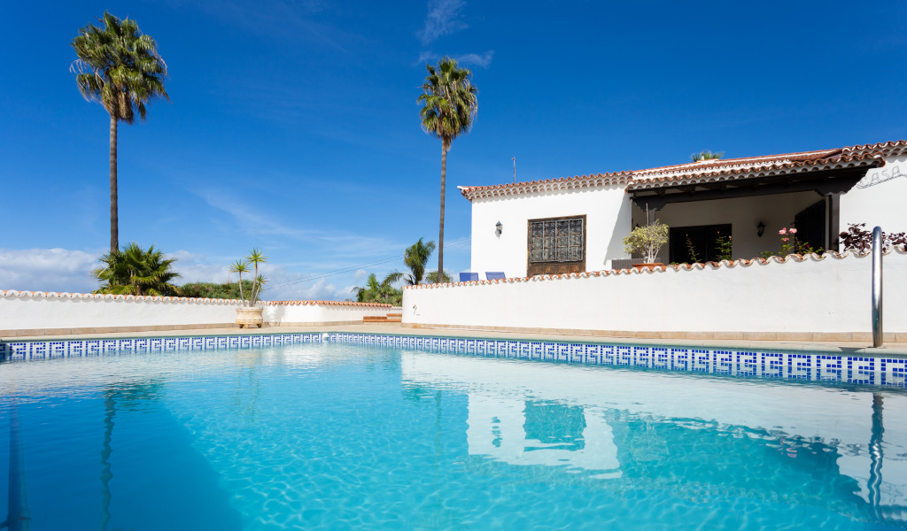 Piscina e casa con palme a Tenerife sotto cieli azzurri.