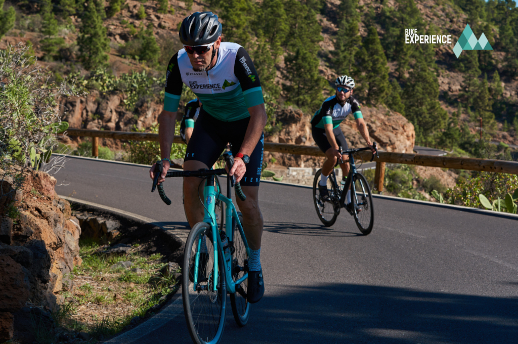 Ciclisti su una strada montuosa a Tenerife, paesaggio boschivo sullo sfondo.
