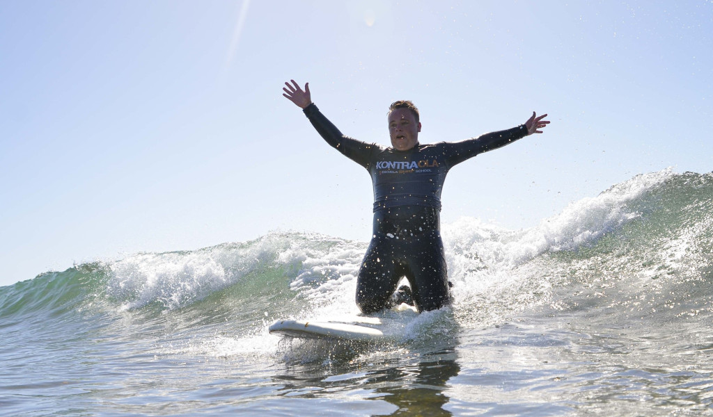 Surfista sull'onda con le braccia tese, maglietta di Kontraola. Surf a Tenerife.
