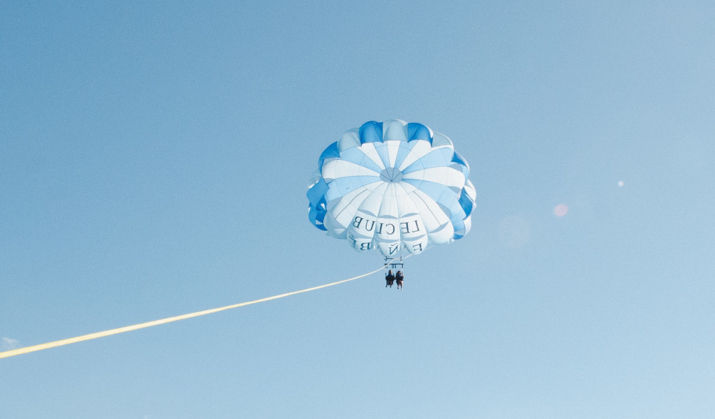 Parasailing nel cielo di Tenerife con persone sotto paracadute bianchi e blu.