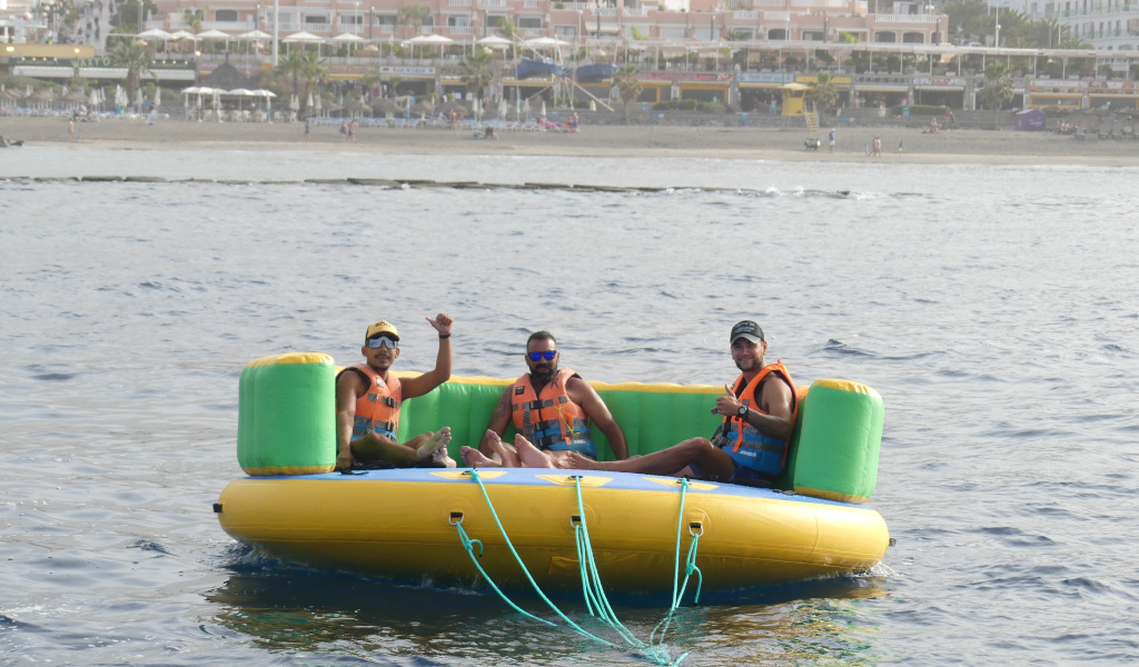 Tre persone su una piattaforma gonfiabile in mare, Playa de las Americas sullo sfondo, Tenerife.
