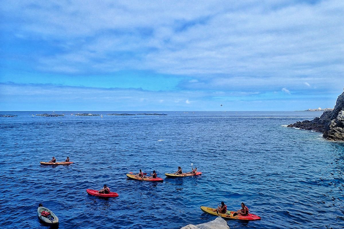 Diverse persone fanno kayak sulla costa di Tenerife sotto un cielo parzialmente nuvoloso.
