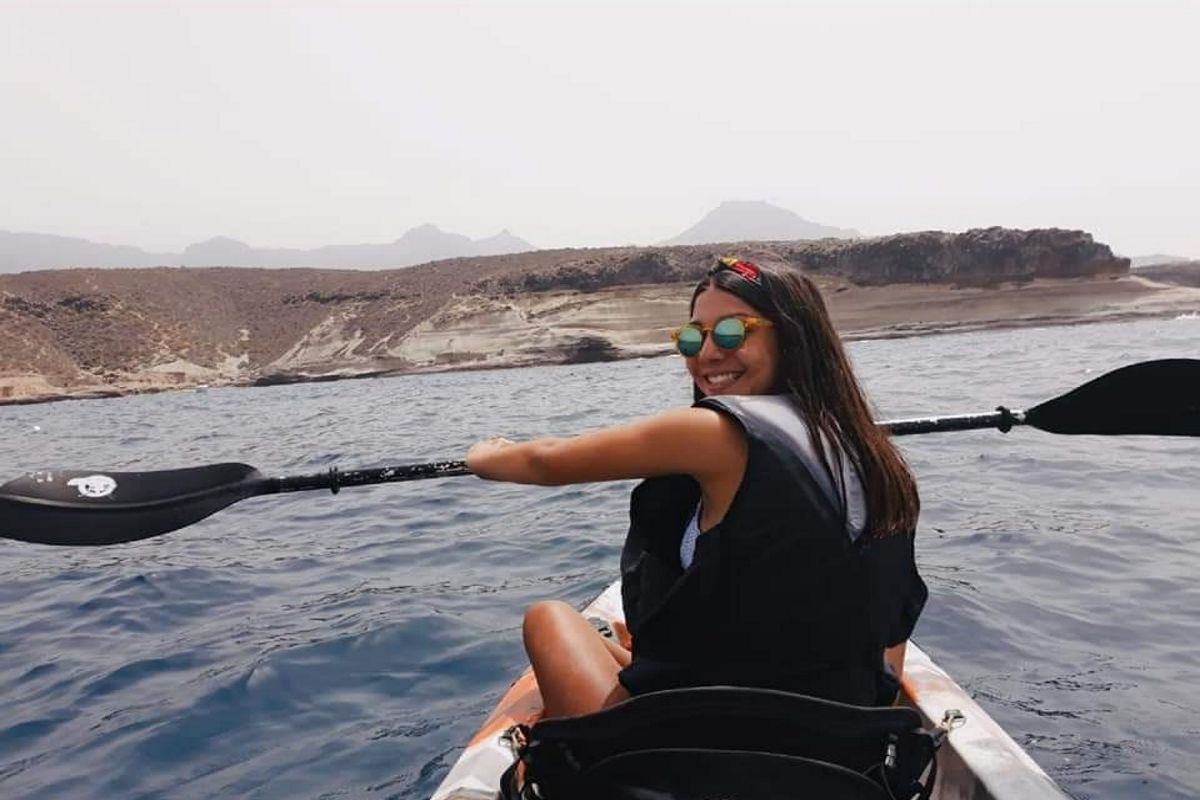 Persona che rema in kayak nelle acque di Tenerife, con paesaggi montuosi sullo sfondo.