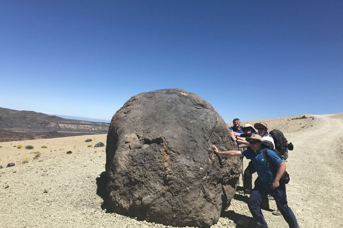 Persone che spingono una grande roccia nel paesaggio vulcanico del Parco Nazionale del Teide, Tenerife.