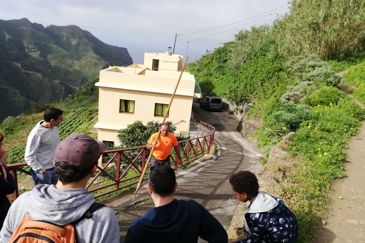 La gente osserva un uomo con un bastone su una strada tra le montagne di Tenerife.