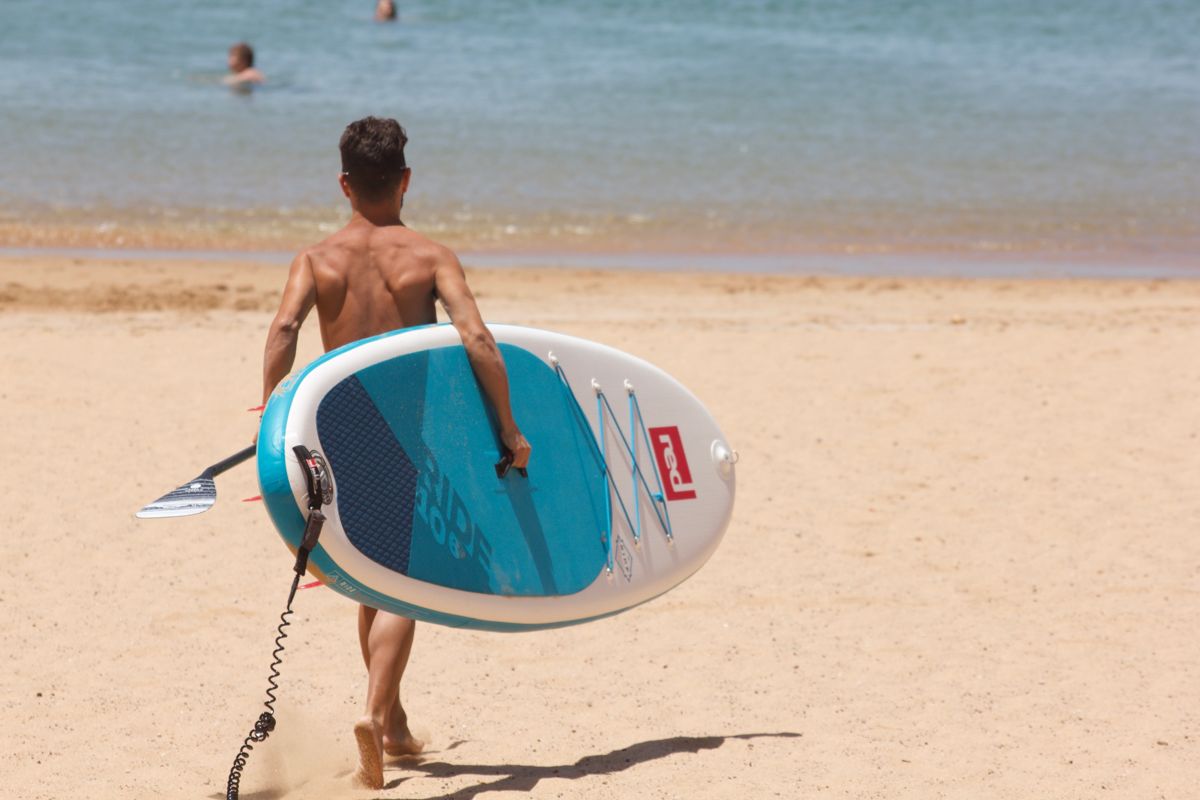 Persona che cammina con una tavola di paddle sulla spiaggia a Tenerife.
