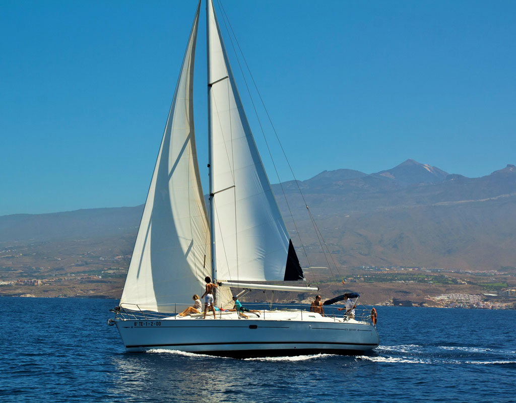 Barca a vela che naviga al largo della costa di Tenerife con montagne sullo sfondo.