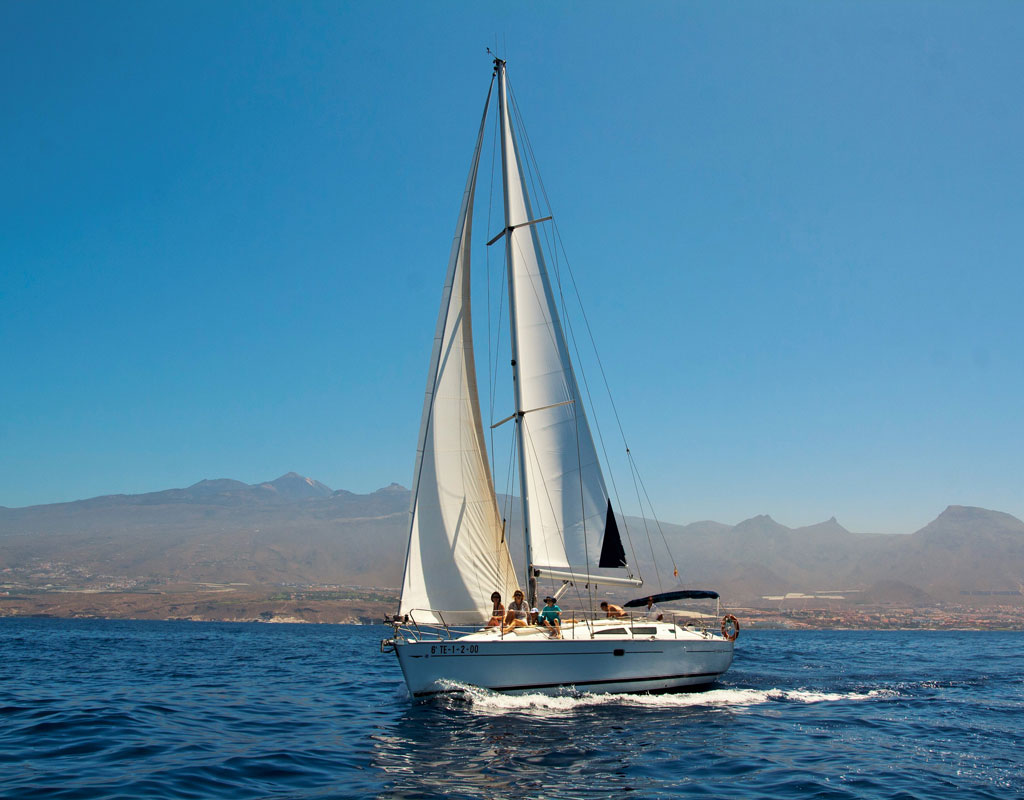 Barca a vela che naviga al largo della costa di Tenerife con montagne sullo sfondo.