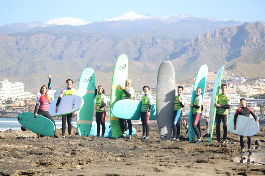 Gruppo di surfisti con tavole sulla spiaggia di Tenerife, montagne sullo sfondo.