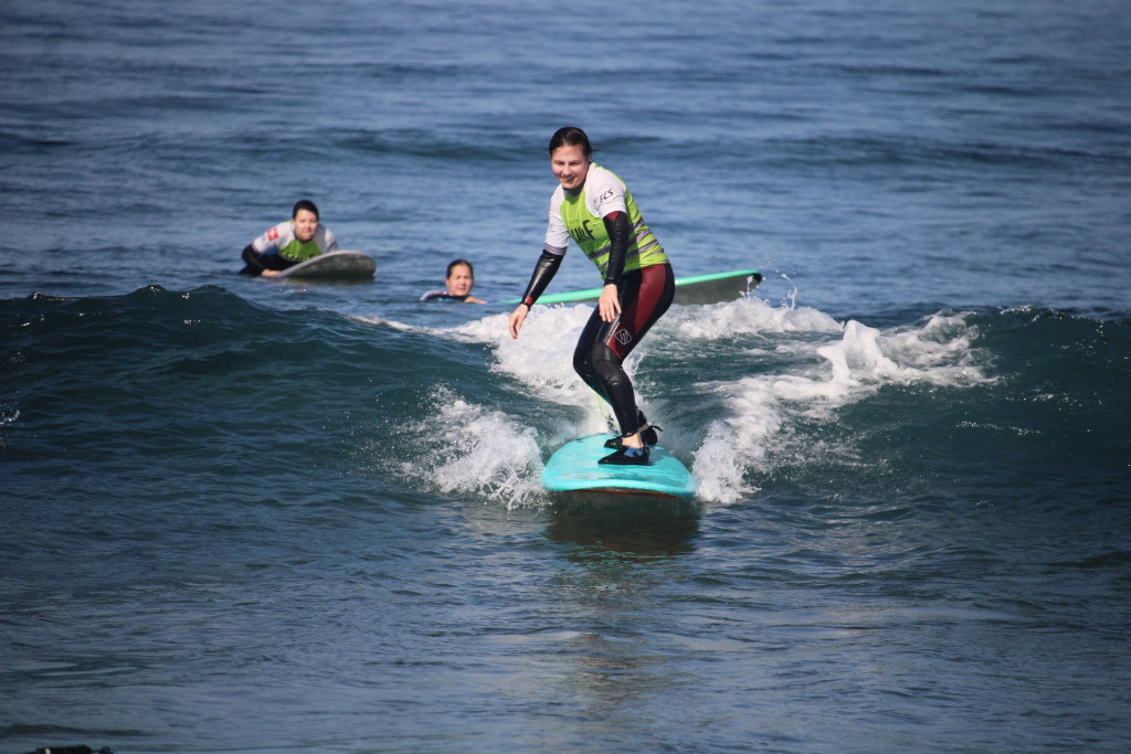 Surfista che cavalca un'onda a Punta del Hidalgo, Tenerife, con due persone sullo sfondo.