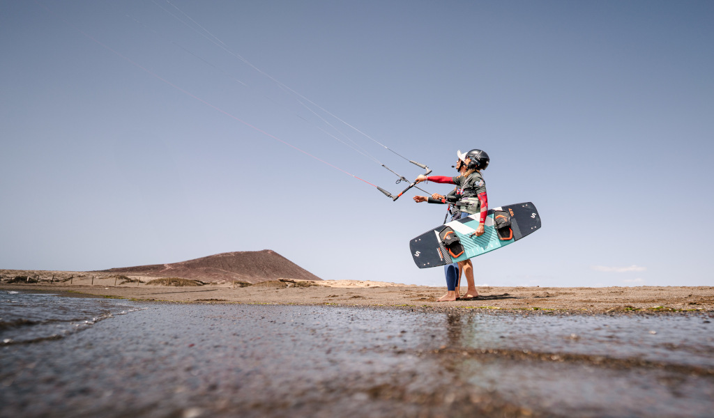 Persona che pratica kitesurf a Playa El Médano, Tenerife, con una collina sullo sfondo.
