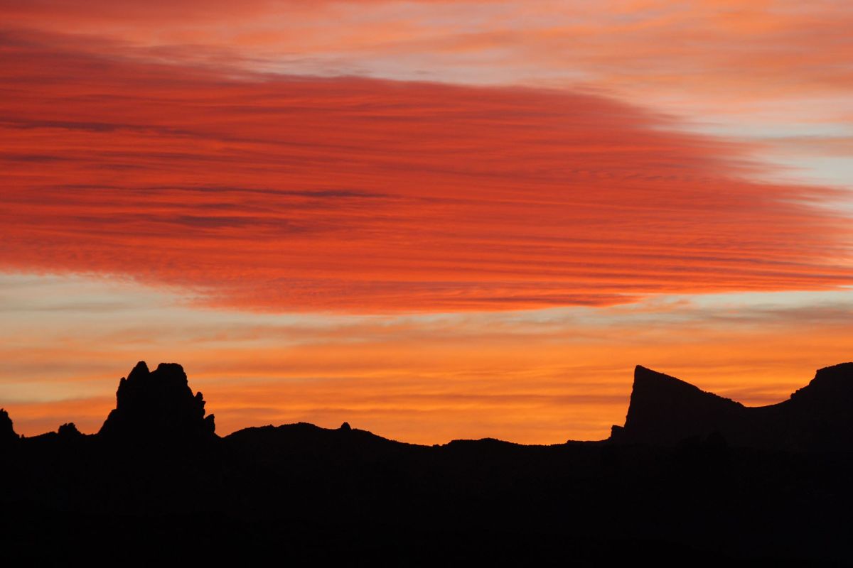 Tramontare sulle montagne di Tenerife con nuvole rosse e cielo arancione.