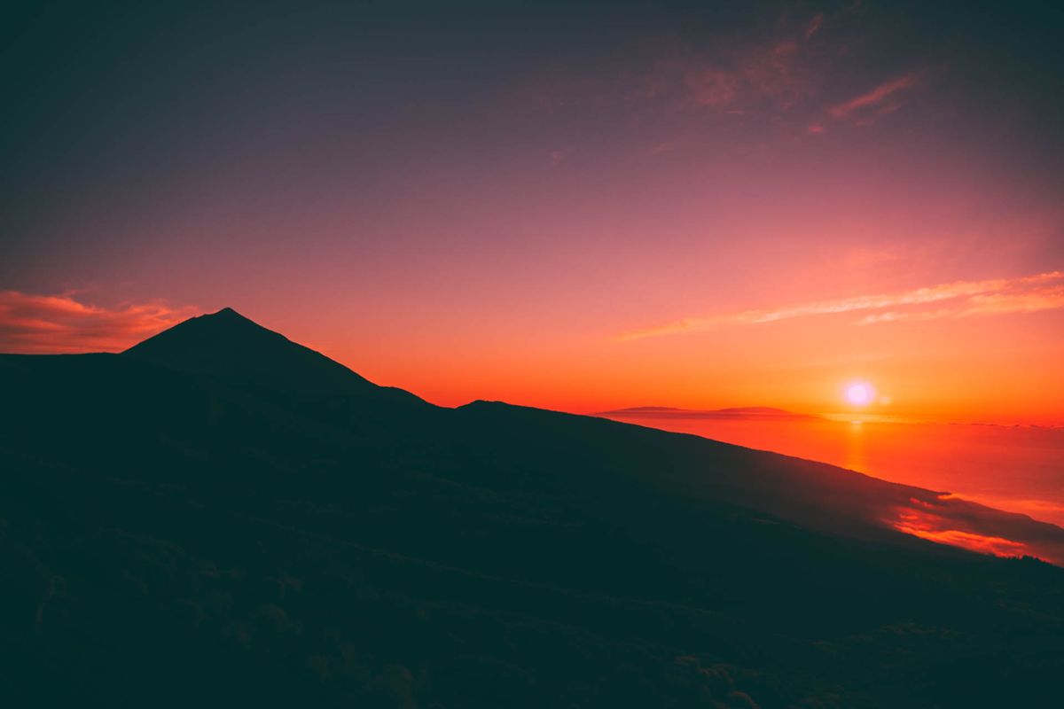 L'alba sul Monte Teide a Tenerife con cieli rossi e sole all'orizzonte.