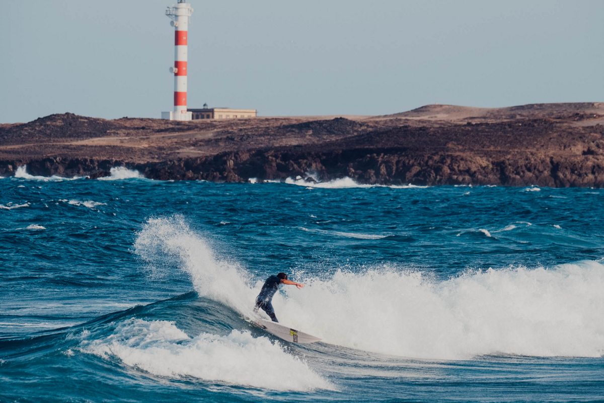 Surfista che cavalca un'onda davanti al faro di Punta de Hidalgo, Tenerife.