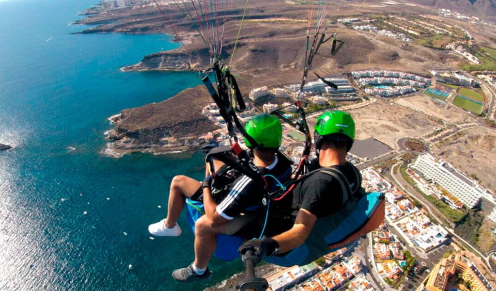Persone che parapendiano sulla costa di Tenerife con vista aerea sul mare e sugli edifici.