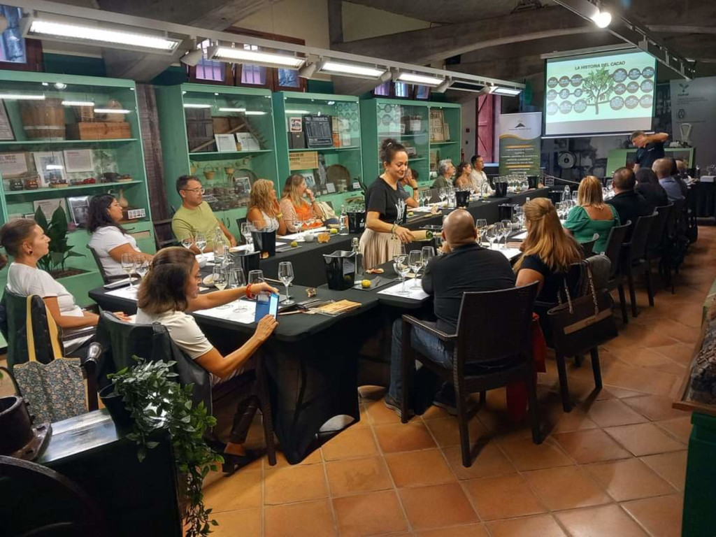 Persone a una degustazione di vini in una sala decorata a Tenerife. Testo visibile: L'anatomia del cacao.