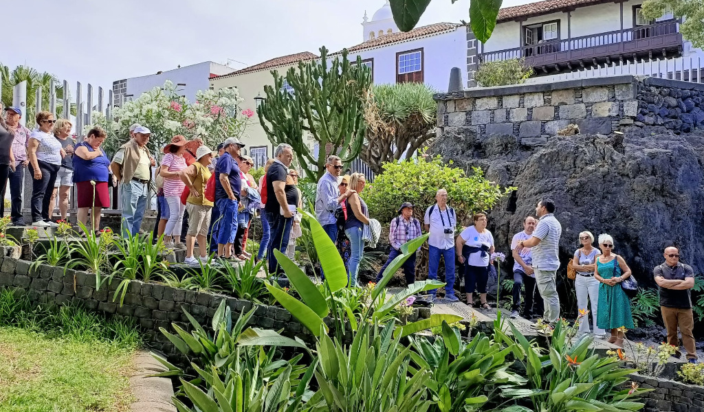 Gruppo di persone che cammina in un giardino in un luogo di Tenerife, circondato da piante e dall'architettura locale.