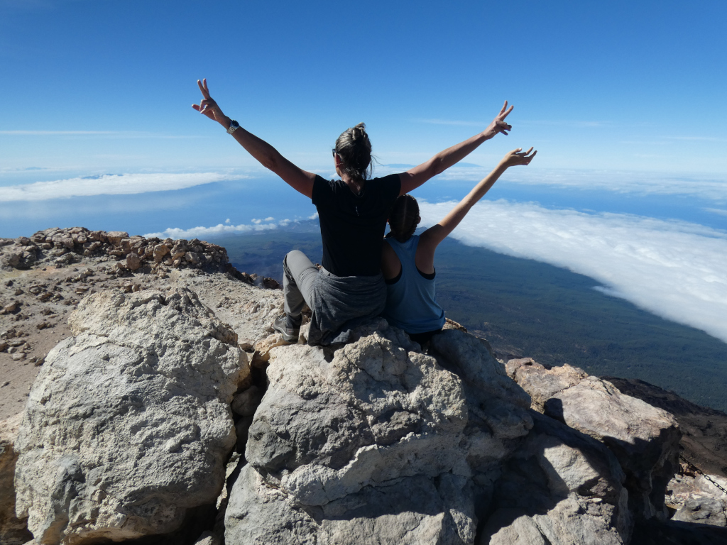 La gente alza le braccia sulla cima del Monte Teide a Tenerife, che osserva il paesaggio nuvoloso.