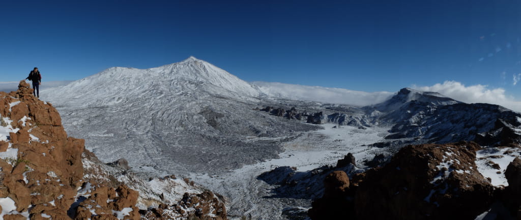 Paesaggio innevato del Monte Teide a Tenerife con un escursionista in cima a una roccia.