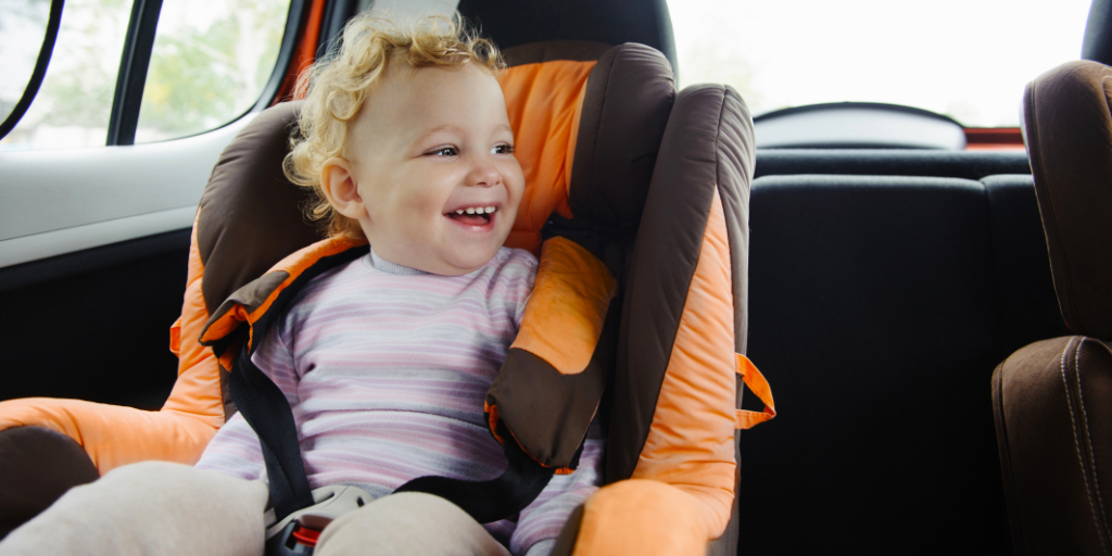 Bambino che sorride su un seggiolino dentro un'auto.