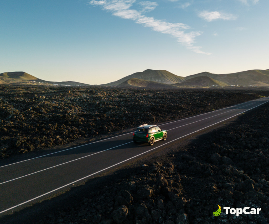 Auto verde che guida sulla strada tra paesaggi vulcanici a Tenerife. Logo TopCar.