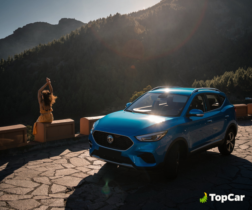 Auto blu davanti alle montagne a Tenerife, donna seduta sul muro sotto il sole.